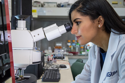 woman wearing a lab coat looking into a microscope